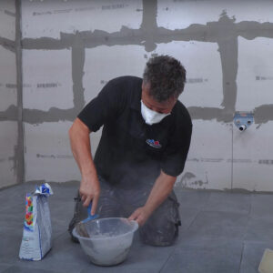 Mixing powder grout with water to create grout to use across floor tiles.