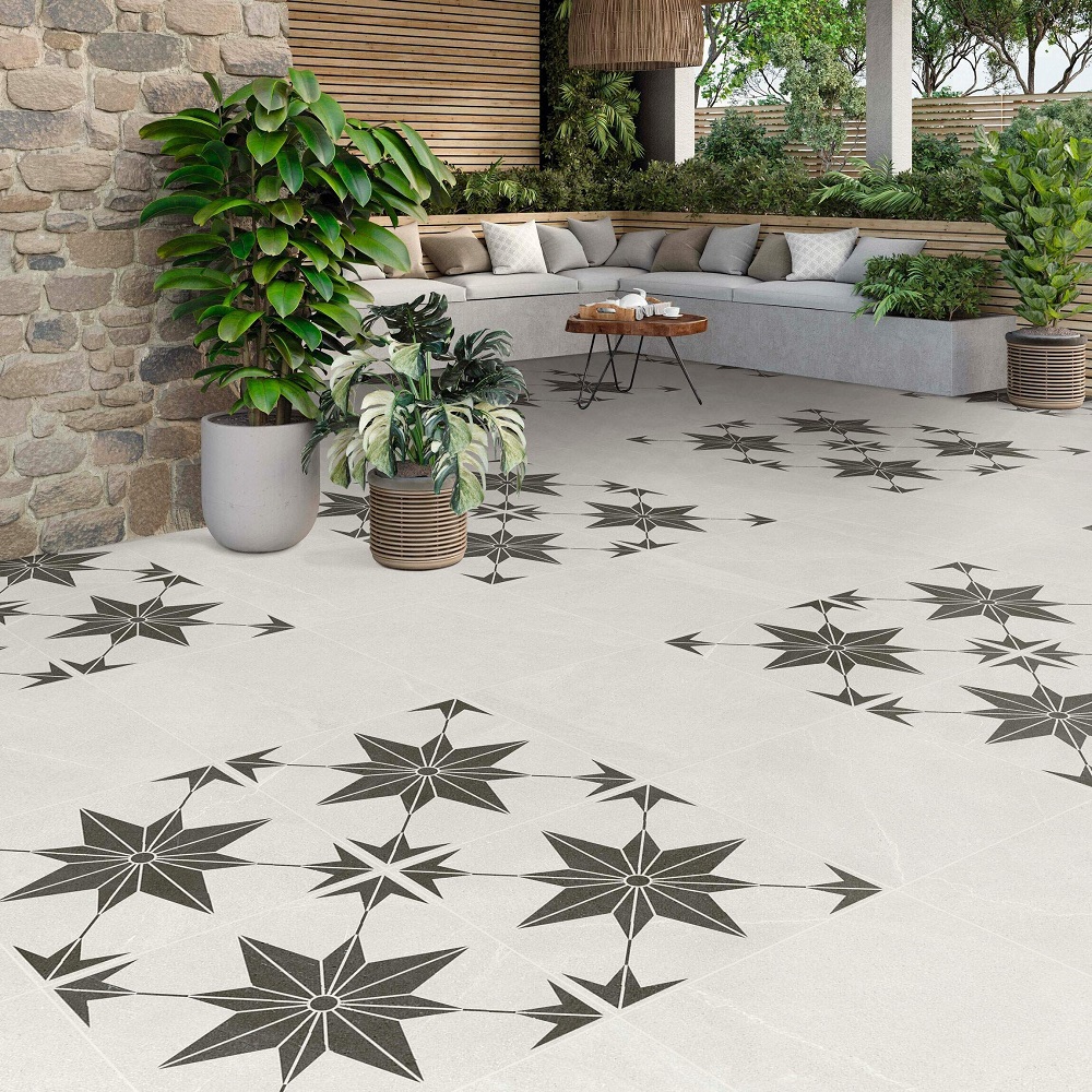 A tranquil patio oasis featuring matt stone effect porcelain tiles adorned with a striking star pattern in a contrasting dark tone, complemented by lush greenery in stylish planters and a cosy corner sofa with a wooden coffee table. 