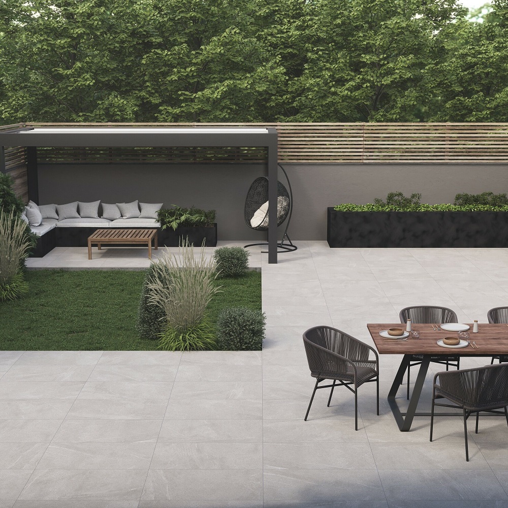 A modern outdoor patio area featuring grey porcelain slabs, furnished with a sleek wooden dining set and a cosy lounge area under a pergola, surrounded by lush greenery and contemporary garden planters. 