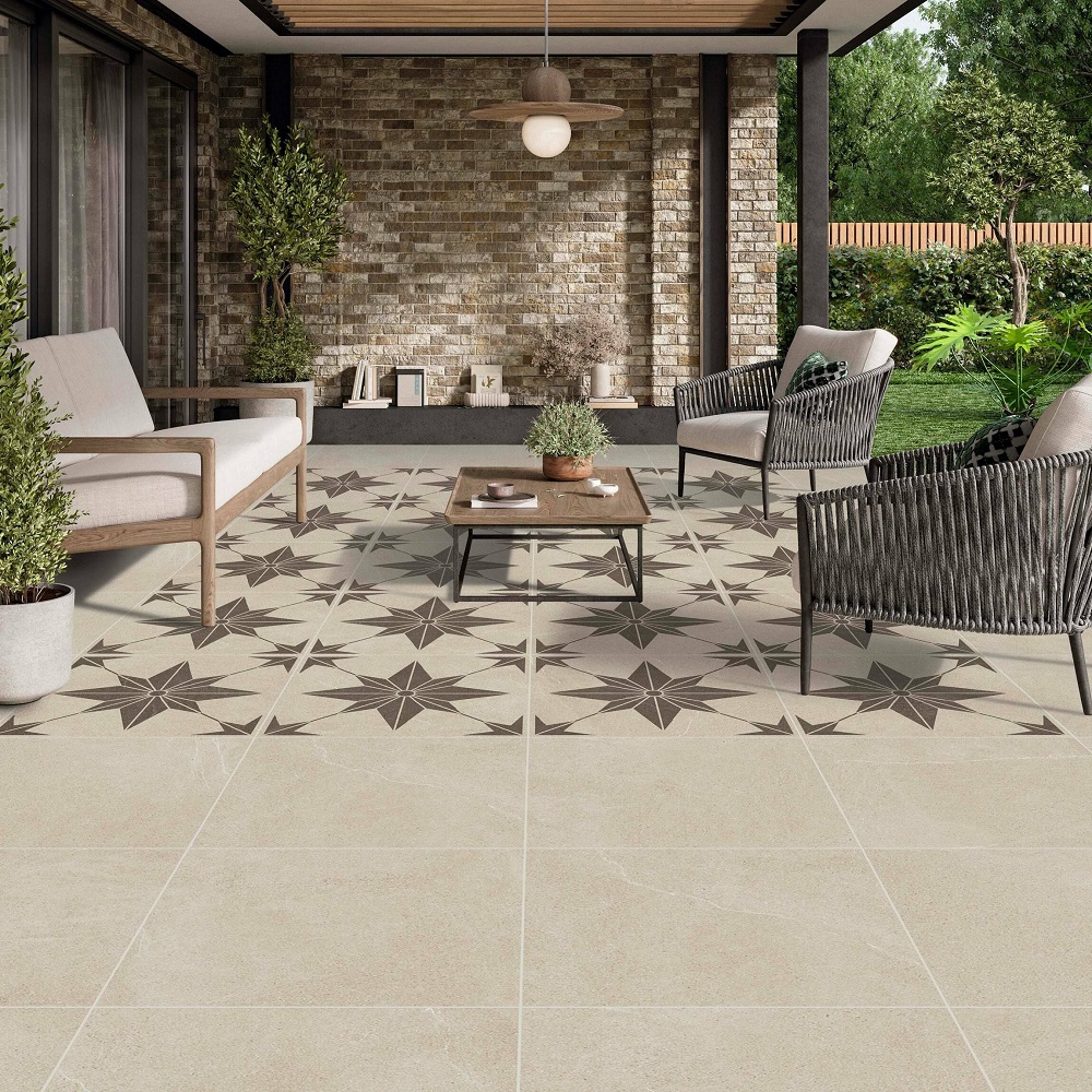 A spacious outdoor patio area with ivory matt stone effect porcelain slabs featuring an intricate star pattern, Modern furniture including a sofa, armchairs and a wooden coffee table complements the natural stone brick wall of the house. The are is adorned with potted plants, under a covered patio with a view of a green garden.