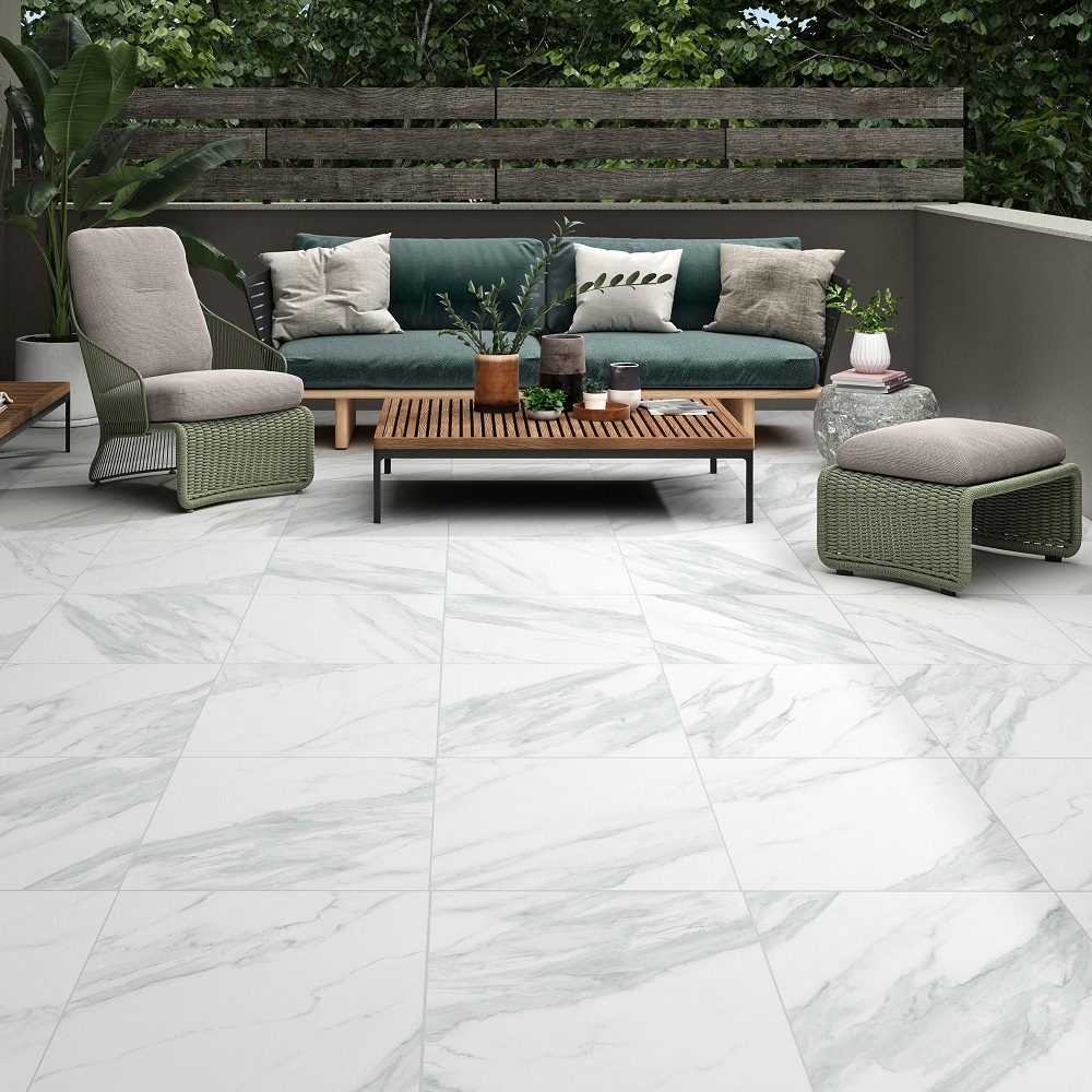 A chic outdoor living space featuring large, glossy porcelain tiles with a white marble effect. The area is furnished with a contemporary deep green outdoor sofa adorned with patterned cushions, a stylish wood and metal coffee table, and a coordinating armchair and footstool with green woven details. Potted plants add a touch of nature, enhancing the tranquil ambiance of this urban garden oasis. 