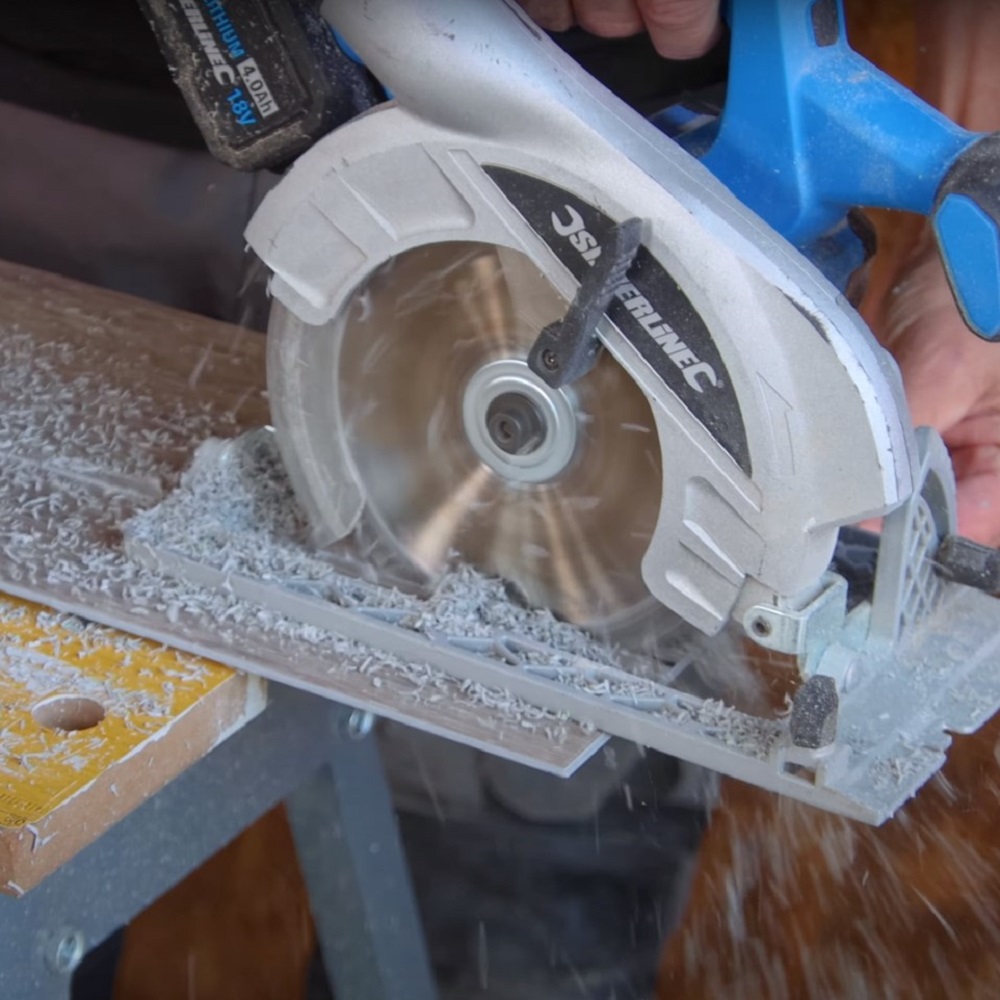 The image captures a close up of a circular saw cutting through an LVT plank, with sawdust particles scattered in the air, highlighting the action of the cut. 